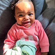 Riley a rejoint le concours — aidez-le/la à gagner de superbes lots ! baby, child, smiling, pink_clothing, blanket, hair_buns, face, hand, indoors, chair, sunlight, happy, person, portrait, cute, cozy, infant, skin, sitting, warm_light