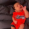 baby, newborn, sleeping, red_clothing, cushion, soft, cozy, infant, cute, peaceful, resting, indoors, child, portrait, small_hands, small_feet, black_hair, casual_wear, relaxed, comfortable