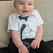 Ophélien participe au concours pour gagner de l'argent avec cette photo : baby, child, smiling, sitting, shirt, bow_tie, suspenders, couch, cushion, happy, indoors, face, person, cute, infant, clothing, footwear, sock, home, portrait