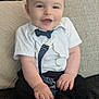baby, child, smiling, sitting, shirt, bow_tie, suspenders, couch, cushion, happy, indoors, face, person, cute, infant, clothing, footwear, sock, home, portrait