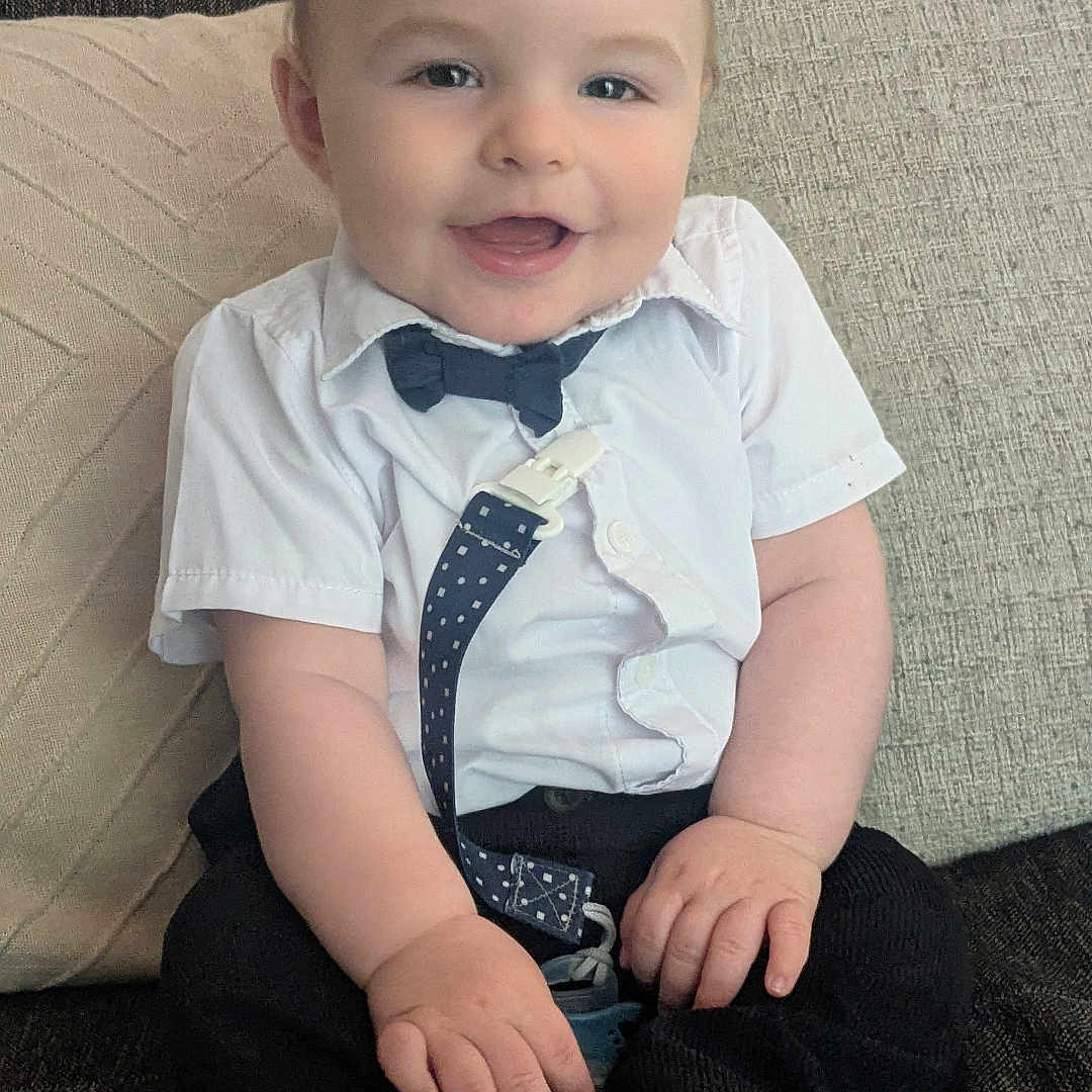Ophélien participe au concours pour gagner de l'argent avec cette photo : baby, bow_tie, child, clothing, couch, cushion, cute, face, footwear, happy, home, indoors, infant, person, portrait, shirt, sitting, smiling, sock, suspenders