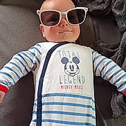 Ethan a rejoint le concours — aidez-le/la à gagner de superbes lots ! baby, sunglasses, onesie, mickey_mouse, striped_clothing, blanket, infant, child, cute, smiling, face, head, person, lying_down, cozy, indoor, soft_texture, clothing, baby_garment, casual