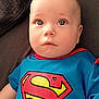 Ethan participe au concours pour gagner de l'argent avec cette photo : baby, child, superman_shirt, blue_clothing, red_clothing, infant, face, eyes, lying_down, fabric, texture, cute, young, portrait, indoors, casual_clothing, person, skin, head, expression