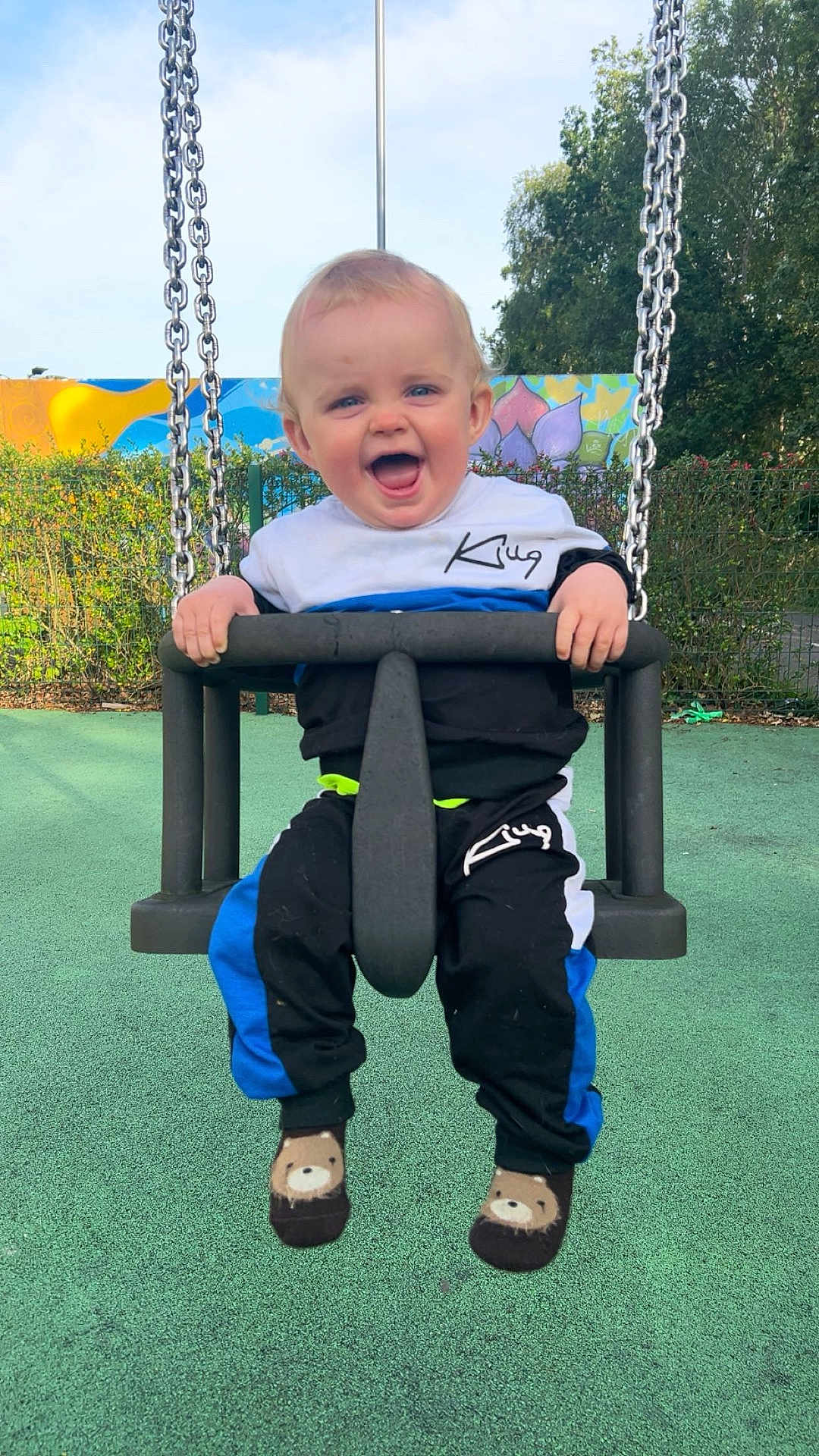 Jayden joined the competition — help win amazing prizes! toddler, child, swing, playground, smiling, happy, outdoor, clothing, socks, bear, chains, greenery, fence, colorful, mural, sky, daylight, fun, person, park