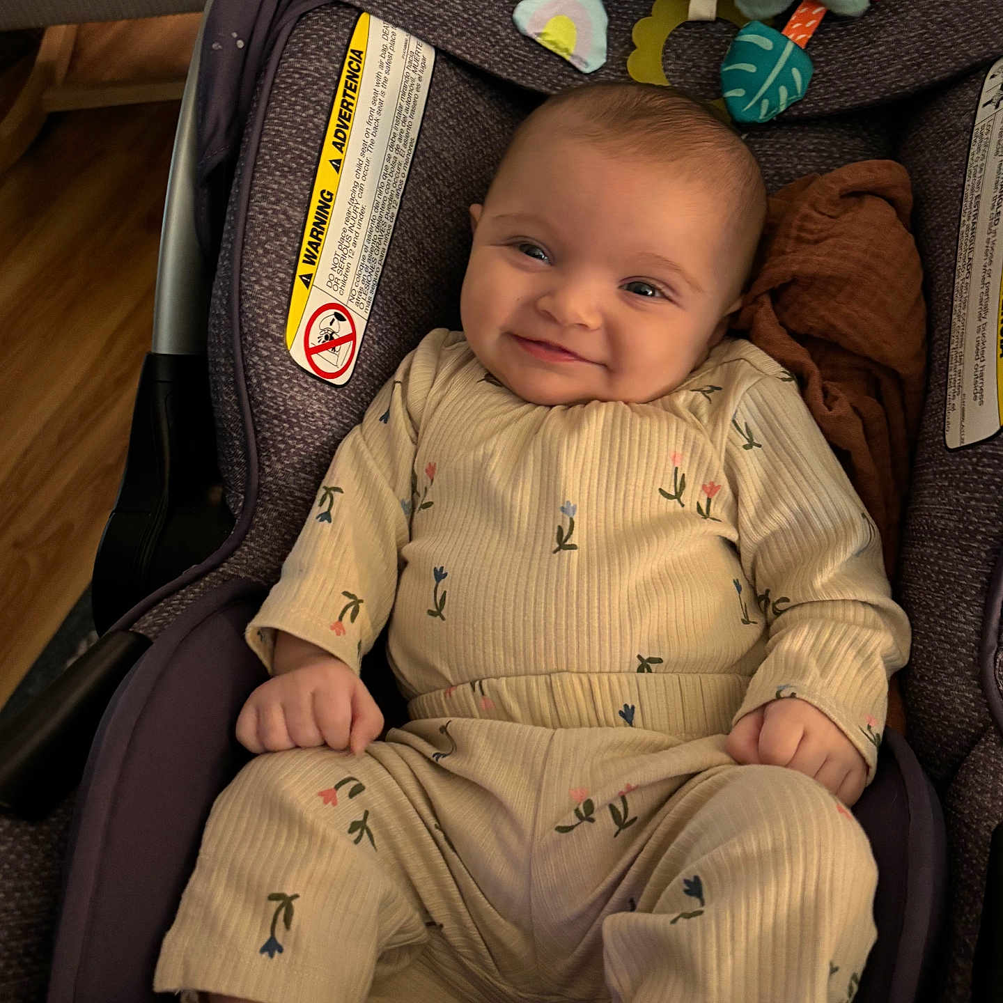 Selena is registered to the contest to win money with this photo: baby, smiling, car_seat, infant, child, cute, clothing, patterned_outfit, soft_toy, indoor, happy, portrait, seat_belt, wooden_floor, fabric, head, face, foot, hand, cozy