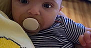 Selena joined the competition — help win amazing prizes! baby, pacifier, striped_clothing, indoor, person, child, face, eyes, hand, flooring, furniture, smiley_face, shirt, holding, closeup, expression, young_child, cute, portrait, comfort