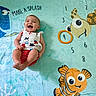 baby, blanket, cartoon_fish, child, clothing, colorful, cute, fun, happy, infant, laughing, lying_down, marine_life, patterned, playful, red_shorts, smiling, star_pattern, turtle, underwater_theme
