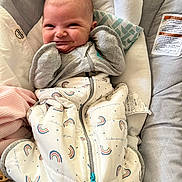 Selena is registered to the contest to win money with this photo: baby, infant, smile, face, clothing, blanket, sleeping_bag, cushion, baby_seat, indoor, cute, child, cozy, pattern, rainbow, zipper, apparel, person, newborn, happy