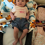 Selena is registered to the contest to win money with this photo: baby, bed, blanket, clothing, colorful, cute, denim, eyes, fabric, face, feet, folded_clothes, hands, indoor, infant, legs, pattern, shirt, soft, text