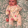 Selena is registered to the contest to win money with this photo: baby, infant, onesie, pacifier, bedspread, pattern, smile, face, clothing, footwear, cute, lying_down, indoor, child, person, soft_toys, bedroom, comfort, happy, small