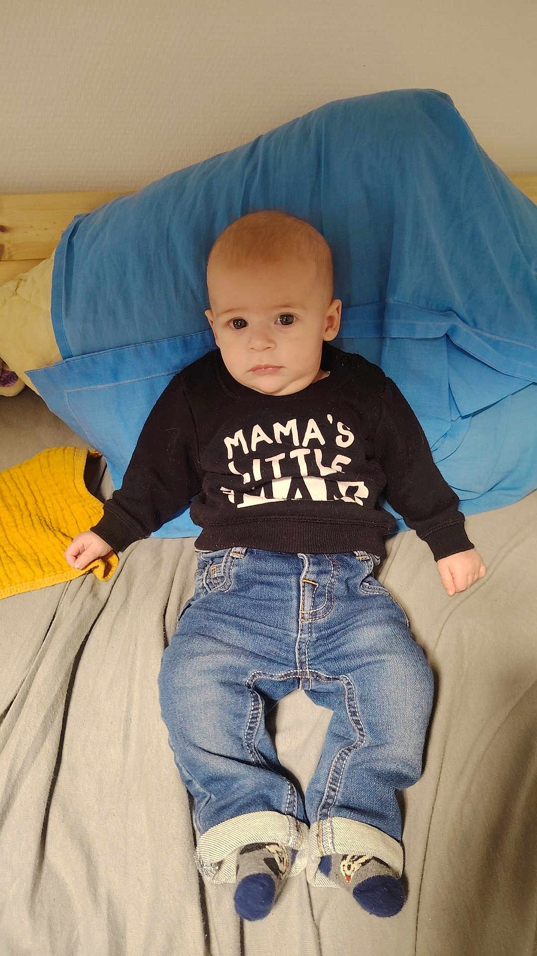 Leo participe au concours pour gagner de l'argent avec cette photo : baby, infant, child, person, clothing, sweatshirt, jeans, socks, bed, pillow, blue_pillow, yellow_towel, indoor, portrait, cute, lying_down, face, expression, casual, young_child