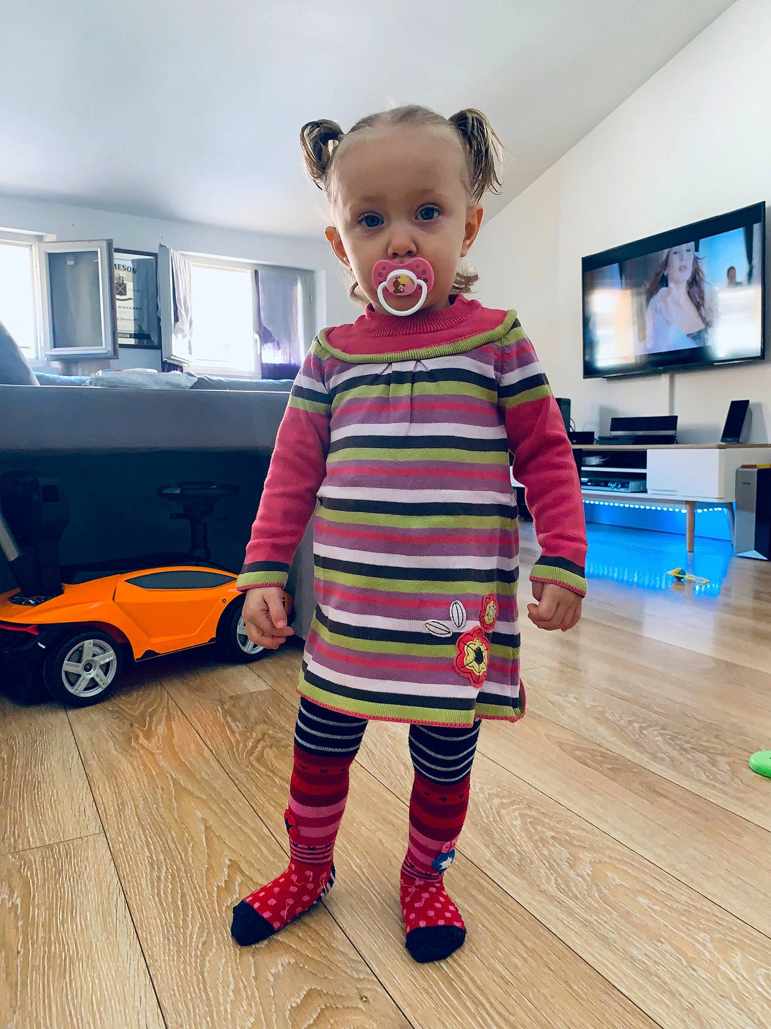 Lèna participe au concours pour gagner de l'argent avec cette photo : baby, baby_toddler_clothing, child, floor, flooring, fun, hardwood, orange, pattern, person, room, sleeve, standing, t_shirt, television, tire, toddler, vehicle_door, wheel, wood