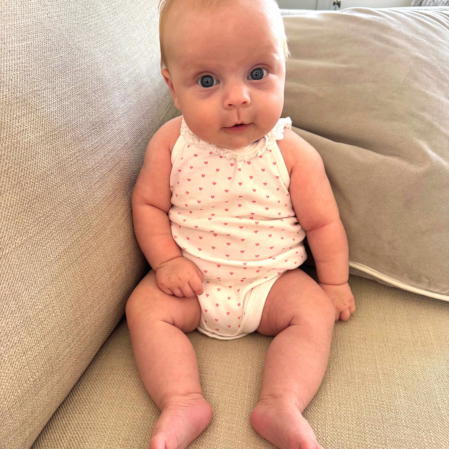 Olivia Glynn is registered to the contest to win money with this photo: baby, beige, child, couch, cute, expression, face, feet, furniture, hands, indoor, infant, legs, onesie, person, pink_hearts, portrait, sitting, skin, young
