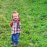 child, toddler, outdoor, grass, field, nature, greenery, trees, sky, clouds, portrait, standing, smiling, plaid_shirt, jeans, red_clothing, long_hair, playful, rural, landscape