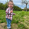 child, cloudy, countryside, cute, daylight, grass, jeans, nature, orchard, outdoor, plaid_shirt, portrait, sky, smiling, snack, sneakers, standing, toddler, topknot, trees
