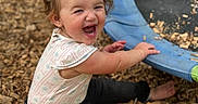 Raelynn joined the competition — help win amazing prizes! barefoot, black_pants, child, daylight, face, happy, laughing, laughter, outdoor, patterned_shirt, play, playground, playground_equipment, ponytail, portrait, recreation, sitting, smiling, toddler, wood_chips
