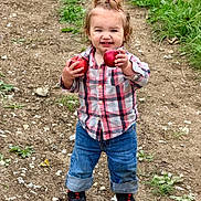 Raelynn joined the competition — help win amazing prizes! child, toddler, smiling, outdoors, apples, fruit, orchard, dirt_path, grass, nature, portrait, standing, plaid_shirt, jeans, sneakers, ponytail, happy, red_apples, facial_expression, daylight