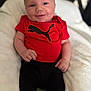 baby, smiling, infant, red_shirt, black_pants, puma_logo, soft_blanket, happy, cute, portrait, indoors, person, child, clothing, hand, face, head, sitting, skin, young