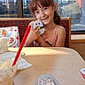 Luna joined the competition — help win amazing prizes! child, smiling, portrait, restaurant, booth, table, plush_toy, toy, drink, straw, dessert, food, window, vehicle, indoor, daylight, brown_hair, pink_shirt, sitting, happy