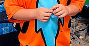 Thade is registered to the contest to win money with this photo: child, boy, smiling, portrait, costume, orange_clothing, blue_clothing, superhero, standing, indoors, bedroom, toys, playroom, carpet, short_hair, happy, full_body, colorful, casual, photography