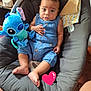 child, baby, infant, blue_outfit, stitch_plush, plush_toy, stuffed_animal, bouncer, baby_seat, cushion, blanket, toy, barefoot, looking_at_camera, big_eyes, seated, indoor, human_face, brown_hair, soft_fabric
