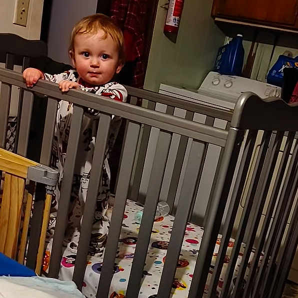 Zauntee Sebastian is registered to the contest to win money with this photo: toddler, child, crib, baby, standing, indoor, laundry, washing_machine, home, furniture, clothing, curious, room, bar, pajamas, face, person, young_child, playpen, baby_bed