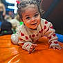 toddler, child, smiling, crawling, red_hair_ties, heart_pattern, sweater, orange_surface, indoor, play_area, cute, happy, portrait, baby, face, person, young_child, warm_lighting, soft_focus, fun