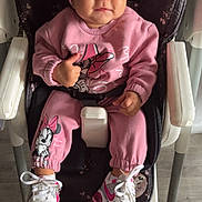 Arya participe au concours pour gagner de l'argent avec cette photo : toddler, child, pink_clothing, headband, flower, high_chair, sneakers, thumbs_up, smiling, indoor, floor, person, cute, baby, mickey_mouse, cartoon_character, footwear, seat_belt, happy, portrait