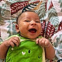 baby, infant, smiling, green_clothing, onesie, dinosaur, happy, lying_down, blanket, patterned_blanket, cute, hand, face, child, indoors, portrait, expression, joy, small_child, human
