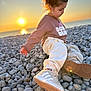 Lonie participe au concours pour gagner de l'argent avec cette photo : child, sunset, beach, pebbles, braids, casual_clothing, sneakers, sea, outdoor, nature, young_girl, side_profile, sunlight, warm_light, relaxed, sitting, portrait, scenic, cozy, daytime