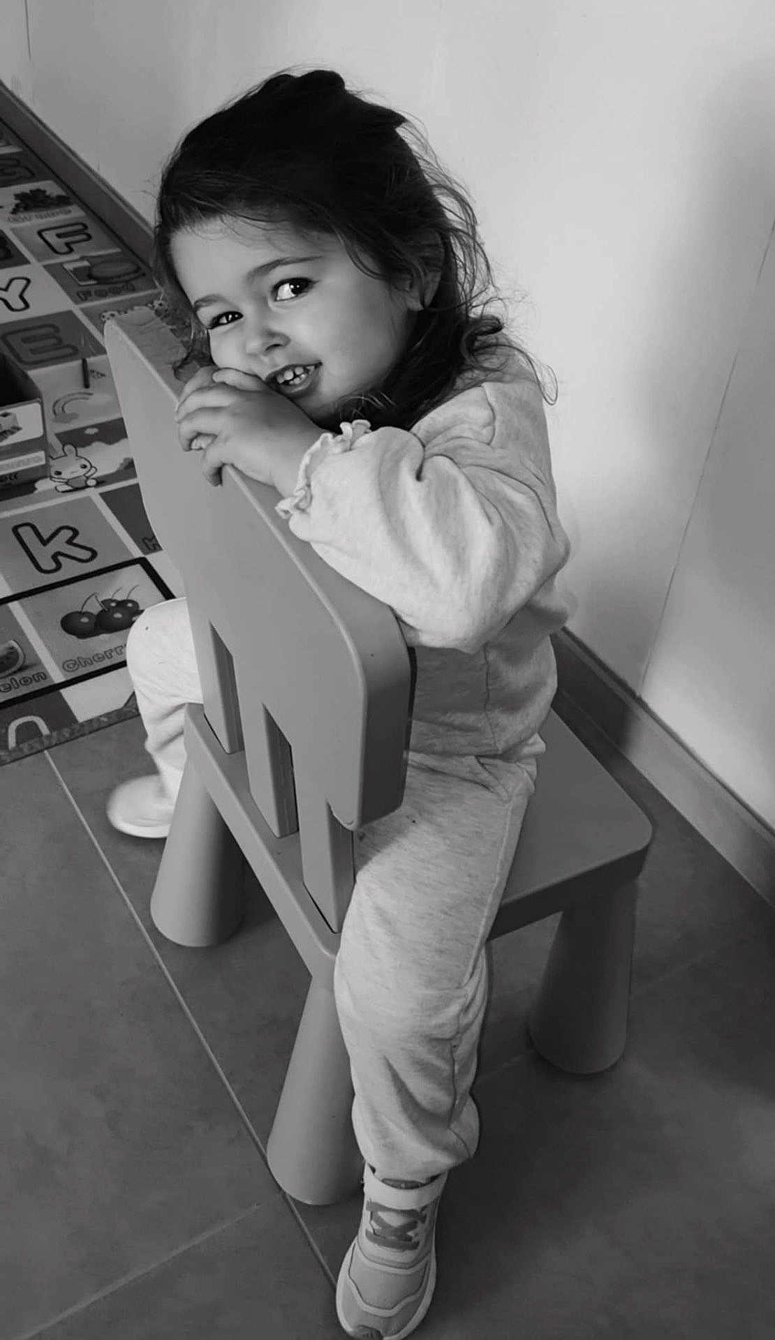 Lonie a rejoint le concours — aidez-le/la à gagner de superbes lots ! child, smiling, chair, indoor, playmat, toy, sneakers, cute, portrait, happy, young, person, floor, clothing, curly_hair, monochrome, toddler, playroom, sitting, cozy