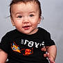 baby, background, black_shirt, child, clothing, curly_hair, cute, eyebrows, face, hand, happy, indoor, infant, person, photography, portrait, sitting, skin, smiling, young