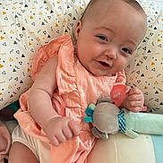 Kenza a rejoint le concours — aidez-le/la à gagner de superbes lots ! baby, child, smiling, infant, dress, pink_clothing, pacifier, soft_toy, pillow, patterned_pillow, geometric_pattern, cute, happy, indoor, person, plush_toy, lying_down, close_up, skin, head