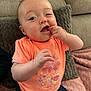 baby, infant, child, orange_shirt, pineapple_design, hand, face, couch, pillow, blanket, sitting, indoor, cute, expression, skin, person, clothing, comfort, playful, portrait