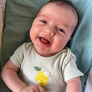 Sage is registered to the contest to win money with this photo: baby, smiling, infant, onesie, cute, happy, face, child, portrait, clothing, sitting, young, skin, hand, cushion, cute_clothing, lying_down, cheerful, indoors, baby_girl