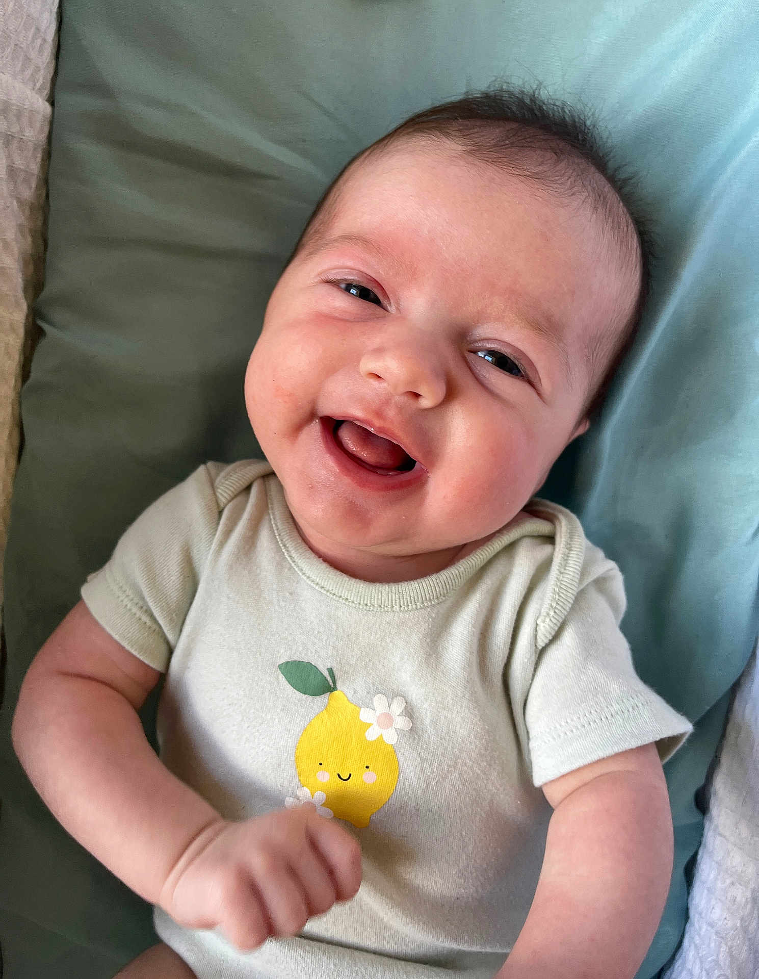 Sage is registered to the contest to win money with this photo: baby, smiling, infant, onesie, cute, happy, face, child, portrait, clothing, sitting, young, skin, hand, cushion, cute_clothing, lying_down, cheerful, indoors, baby_girl