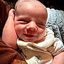Weston is registered to the contest to win money with this photo: baby, smiling, close_up, infant, sleepy, cozy, blanket, clothing, soft_texture, cute, face, arm, resting, indoors, portrait, newborn, happy, skin, person, comfort