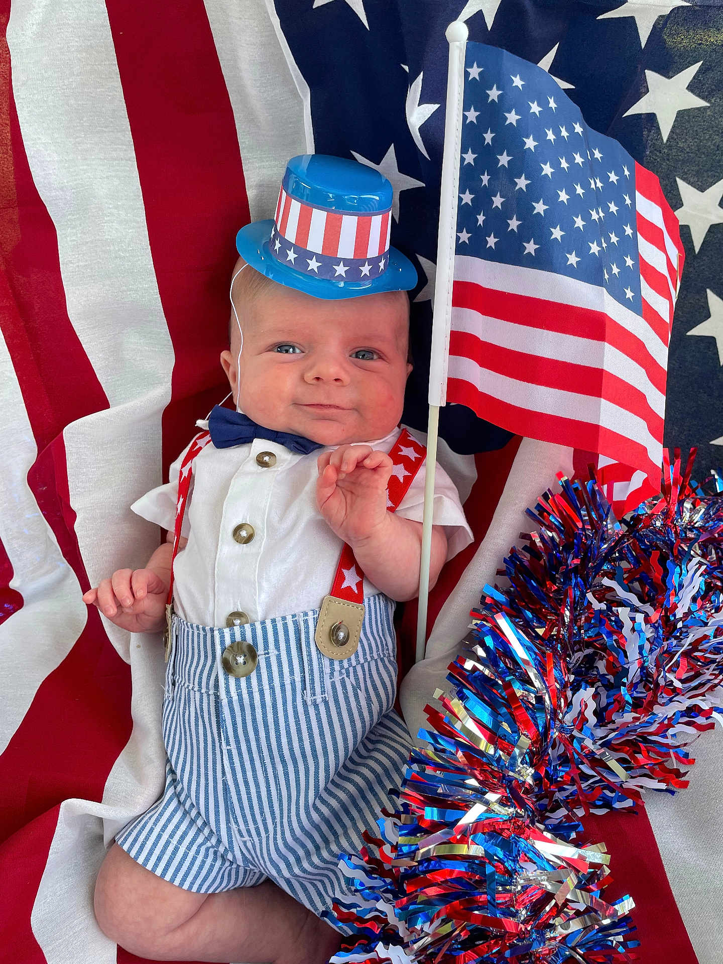 Weston is registered to the contest to win money with this photo: baby, child, patriotic, flag, american_flag, hat, bow_tie, suspenders, striped_shorts, tinsel, red_white_blue, smiling, portrait, celebration, holiday, festive, cute, infant, background, clothing