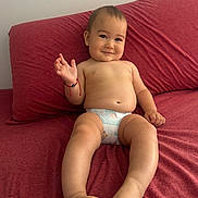 Raiden is registered to the contest to win money with this photo: baby, child, diaper, couch, red_couch, smiling, sitting, bracelet, hand, foot, toes, face, cheeky, indoors, skin, young_child, cute, happy, waving, relaxed