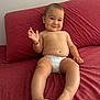 baby, child, diaper, couch, red_couch, smiling, sitting, bracelet, hand, foot, toes, face, cheeky, indoors, skin, young_child, cute, happy, waving, relaxed