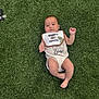 baby, infant, bib, green_carpet, keys, lying_down, cute, chubby_cheeks, apparel, expression, skin, legs, arms, footwear_none, indoors, flooring, child, one_person, young, casual