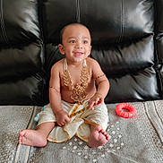 Juhit is registered to the contest to win money with this photo: baby, child, infant, smiling, sitting, portrait, jewelry, gold_necklace, traditional_clothing, white_clothing, leather_couch, toy, teething_ring, indoor, home, barefoot, tilak, happy, closeup, photography