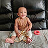 baby, child, infant, smiling, sitting, portrait, jewelry, gold_necklace, traditional_clothing, white_clothing, leather_couch, toy, teething_ring, indoor, home, barefoot, tilak, happy, closeup, photography