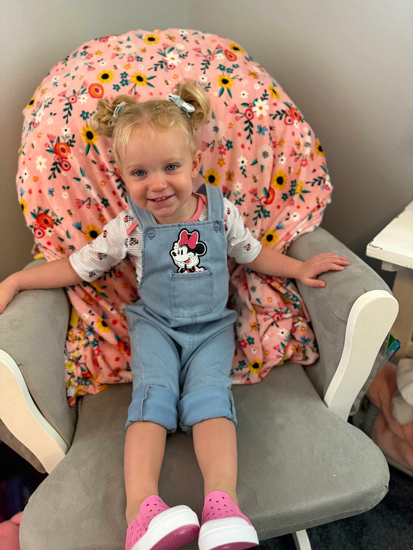 Lily is registered to the contest to win money with this photo: toddler, child, smiling, pigtails, overalls, minnie_mouse, pink_shoes, armchair, blanket, floral_pattern, indoor, happy, cute, person, clothing, hair_bows, seated, portrait, cozy, furniture