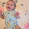 baby, child, smile, happy, onesie, floral, blanket, lying_down, infant, cute, skin, face, hand, arm, leg, pattern, fabric, colorful, indoors, portrait