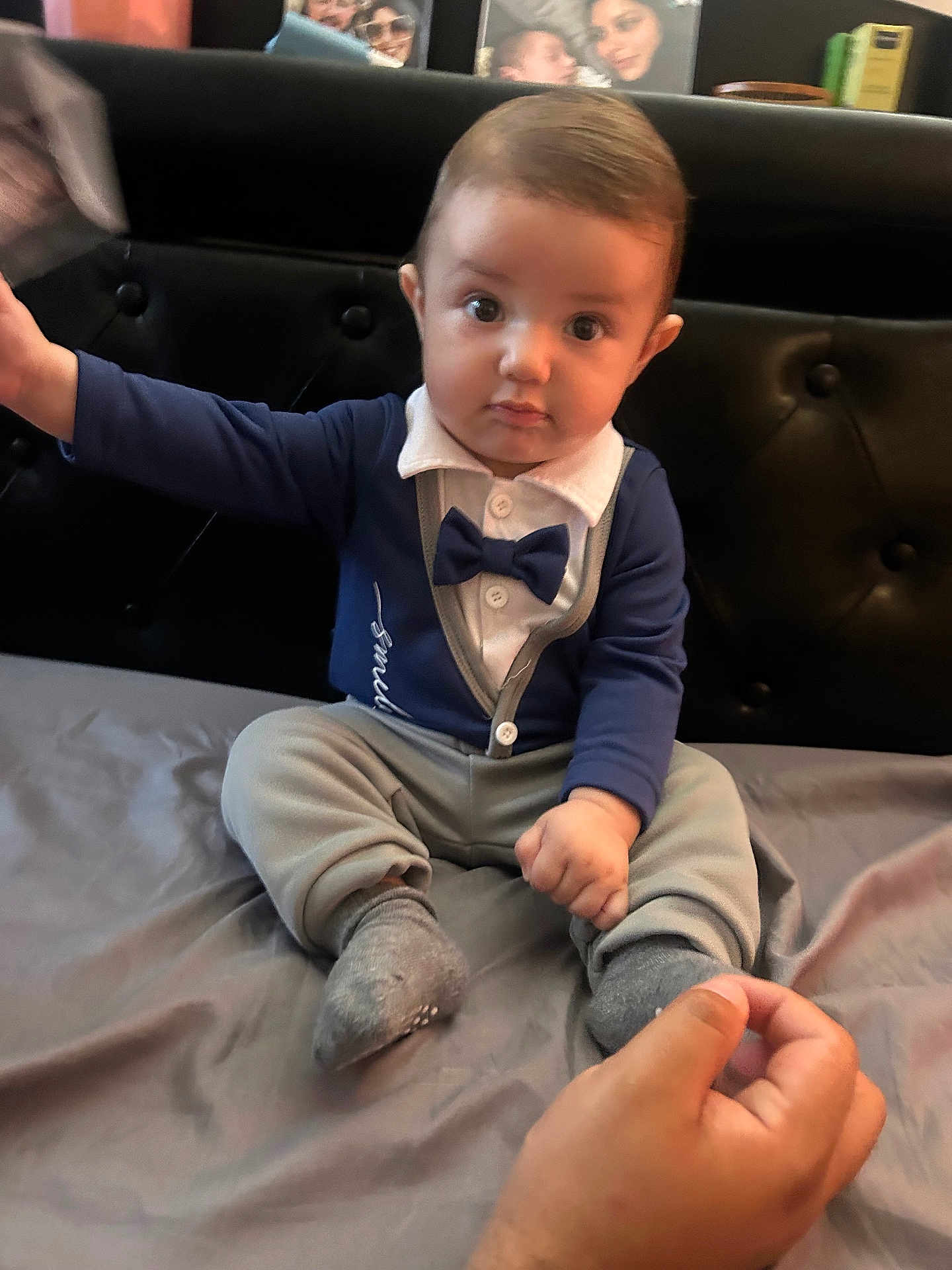 Edi joined the competition — help win amazing prizes! baby, child, infant, bow_tie, blue_clothing, sitting, bed, hand, curious, indoor, portrait, person, headboard, gray_pants, sock, furniture, young_child, cute, engagement, focus
