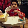 Jose joined the competition — help win amazing prizes! baby, child, high_chair, indoor, portrait, sitting, red_shirt, smiling, face, dark_hair, toy, colorful_toy, table, blanket, couch, air_conditioner, home, wood_floor, family_room, photograph