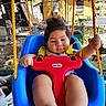 baby, child, infant, swing, outdoor, backyard, smiling, seated, playground, blue_swing, red_safety_bar, yellow_ropes, harness, portrait, face, hands, legs, trees, fence, sunlight