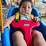 baby, child, infant, swing, playground, outdoor, sitting, safety_harness, red_bar, blue_seat, serious_expression, dark_hair, portrait, close_up, backyard, fence, trailer, play_equipment, summer, photography