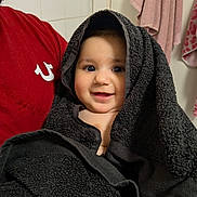 Tanisha joined the competition — help win amazing prizes! baby, child, towel, smile, face, person, indoor, bathroom, red_shirt, black_towel, cute, portrait, happy, wrapped, head_covering, holding, adult, fabric, texture, closeup